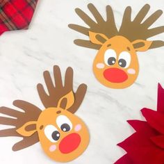 two handprinted reindeer faces on a white marble surface with red and green poinsettis