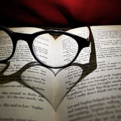 a heart shaped book with reading glasses on it's top and the shadow of an open book behind it