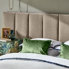 a bed with two green pillows on top of it next to a night stand and nightstand