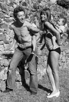 an old black and white photo of two people with a baby in front of a stone wall