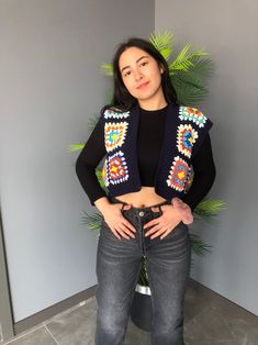 a woman standing in front of a plant with her hands on her hips wearing a black top and jeans