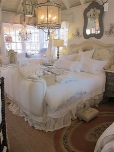 a white bed sitting inside of a bedroom next to a window covered in curtains and pillows