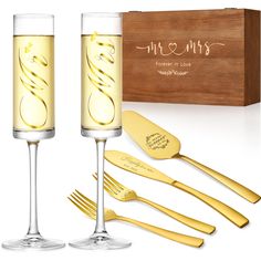 two champagne flutes with gold colored forks and spoons in front of a wooden box