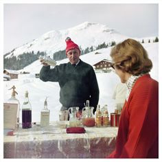 a man and woman sitting at a table in the snow with bottles of liquor on it