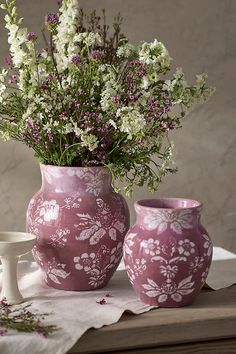 two vases with flowers in them sitting on a table next to an empty cup