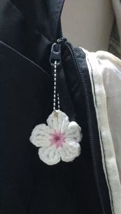 a white crochet flower is attached to a black backpack with a silver ball chain