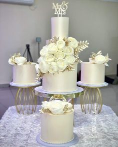 three tiered wedding cake with white roses on top and gold decorations around the edges