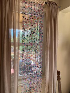 a curtain with beads hanging from it next to a guitar in front of a window