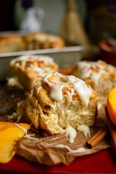 an orange muffin with icing sitting on top of paper next to sliced peaches