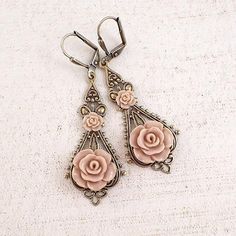 Shabby blush hued resin roses set upon vintage style brass filigree. The roses have a soft semi-matte finish and a very subtle hand-applied metallic bronze sheen. ---------------------------------------------------------------------------------------------Dimensions and details:- From the top of the lever-back ear wires to the bottom of the earrings, they measure approximately 2.3 inches (59mm)- Filigree is antiqued brass, made in the USA- Roses are made of resin- Ear wires are antiqued brass, l Vintage Rose Gold Flower Earrings, Vintage Rose-colored Jewelry For Weddings, Vintage Rose Wedding Jewelry, Elegant Adjustable Rose Design Earrings, Vintage Rose Flower Jewelry, Vintage Rose-colored Flower-shaped Jewelry, Vintage Rose Gold Flower Earrings Gift, Antique Pink Earrings For Weddings, Vintage Pink Nickel-free Flower Earrings