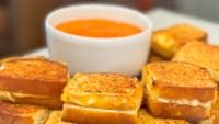 toasted sandwiches on a plate with a bowl of tomato soup in the middle and bread cut into cubes