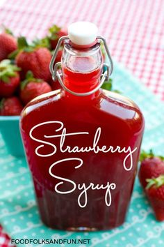 a bottle of strawberry syrup sitting on top of a table next to some strawberries