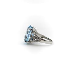 This is part of Chairish’s Fine Jewelry assortment.  This 14k white gold, diamond, and blue topaz ring contains a striking 19+ carat vibrant blue gemstone. The oval stone is beautifully cut with facets that reflect a myriad of Mediterranean blue magic. An elaborate, scrolling foliate pattern details the carriage of the ring, and a triad of diamond lines add sparkle to each side of the topaz—perfect against the 14k white gold. The blue topaz has mesmerising depth to its sparkle, like a pool of wa Formal Blue Topaz Platinum Ring, Blue Topaz Ring With Diamond Accents In Platinum, Platinum Blue Topaz Ring With Diamond Accents, Blue Topaz Ring In Platinum, Oval Blue Topaz Ring With Diamond Cut, Blue Oval Topaz Ring In Art Deco Style, Oval Topaz Ring In Platinum, Art Deco Oval Topaz Ring With Center Stone, Classic Platinum Topaz Ring With Accent Stones