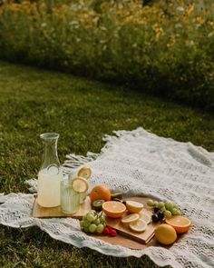 a glass bottle and some fruit on a blanket in the grass with flowers behind it