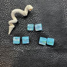 four pieces of blue glass sitting on top of a black leather surface next to a white ribbon