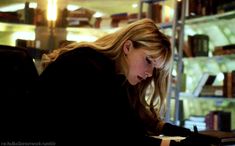 a woman sitting at a table with a laptop computer in front of her and bookshelves behind her