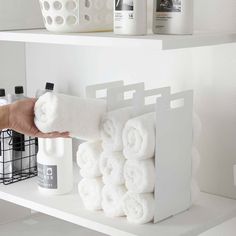 a person is holding some white towels in front of the bathroom shelf with other items on it