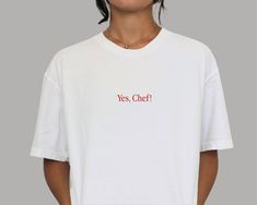 Welcome to Apéro Apparel! Spice up your wardrobe with our exclusive retro-style vintage-fit unisex t-shirt, featuring the slogan "Yes, Chef!". This trendy unisex cut looks great on both women and men. Crafted with 100% high-quality midweight cotton, it's soft to the touch, extra comfy, and durable.   Whether you're a Michelin-star chef, a culinary enthusiast, or just someone who loves to eat, this shirt is sure to add a dash of flavor to your fit. Featuring a classic crew neckline, premium ultra-soft feel, and relaxed fit, it's the perfect addition to your streetwear wardrobe essentials.   Product Details:   * Made with 100% midweight 6.1oz cotton * Soft-to-the-touch feel for ultimate comfort * Pre-shrunk for a consistently great fit * Classic crew neckline for a timeless look * Tear-away White T-shirt With Funny Text For Streetwear, Unisex Retro T-shirt With Text Print, Unisex Slogan Crew Neck Top, Short Sleeve Relaxed Fit Shirt With Text Print, Relaxed Fit Short Sleeve Shirt With Text Print, Retro Crew Neck T-shirt With Text Print, Basic Unisex Crew Neck Shirt, Unisex Text Print Crew Neck T-shirt, Unisex Crew Neck T-shirt With Text Print