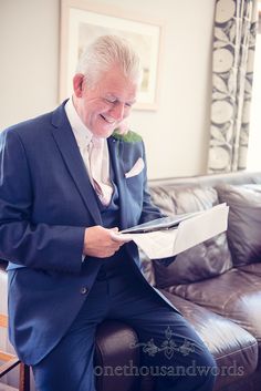 an older man in a blue suit sitting on a couch reading a piece of paper