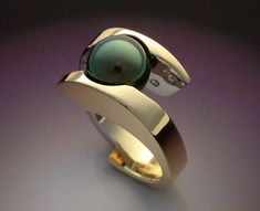 This is a very bold woman's ring in 18k yellow gold and platinum featuring a beautiful, 10.25 mm cultured Tahitian Black Pearl and .29 carat in Diamonds. The Diamonds are flush mounted on either side of the Pearl on the inside of the ring, which is highly polished platinum, while the rest of the ring is 18k yellow gold. the polished platinum and diamonds contrast wonderfully with the Black Pearl and yellow gold. This ring weighs 26 grams total , is 12.6 mm at the top and 8 mm at the back of the Modern Yellow Gold Pearl Ring For Anniversary, Modern Yellow Gold Pearl Ring For Formal Occasions, Modern Diamond Pearl Ring For Anniversary, Modern Wedding Pearl Ring, Luxury Tahitian Pearl Ring For Formal Occasions, Formal Yellow Gold Tahitian Pearl Ring, Gold Tahitian Pearl Rings For Wedding, Elegant Yellow Gold Tahitian Pearl Rings, Modern White Gold Pearl Ring With Polished Finish