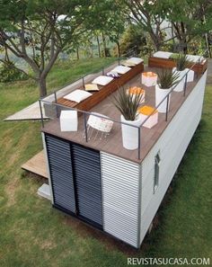 an elevated deck with chairs and tables on it in the grass next to some trees