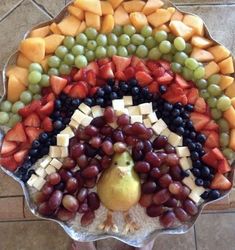 a platter filled with grapes, pears, apples and cheese on top of a tile floor