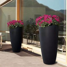 two large black vases with pink flowers in front of a glass window on a patio