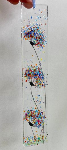 a hand is holding a glass piece with flowers painted on it and confetti sprinkles all over the bottom