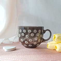 a coffee cup sitting on top of a table next to yellow flowers