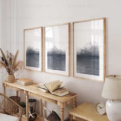 three framed pictures hang on the wall above a wooden table with a lamp and books