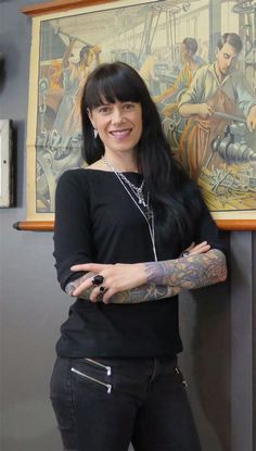 a woman standing next to a wall with tattoos on her arm and arms, smiling at the camera