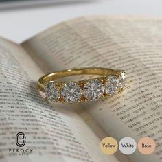 three stone ring sitting on top of an open book with the words yellow gold written below it