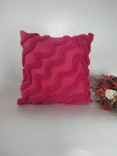 a pink pillow sitting on top of a white table next to a vase with flowers