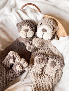 two crocheted teddy bears laying next to each other on a white blanket with a basket