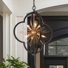 a chandelier hanging from the ceiling in a room with potted plants and windows