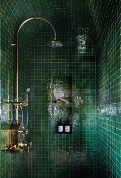 a green tiled bathroom with gold fixtures and shower head in the corner, along with two soap dispensers