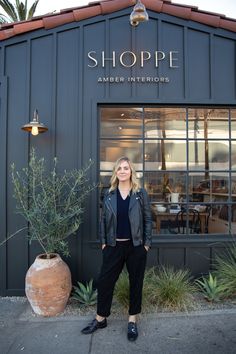 a woman standing in front of a shoppe with plants and potted planters