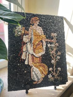 a mosaic is displayed on a table next to a potted plant