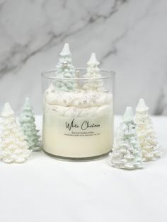 white christmas trees in a glass jar next to some candles on a marble countertop