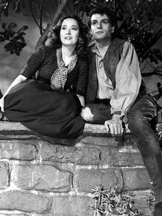 an old black and white photo of a man and woman sitting on a brick wall