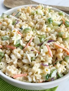 a white bowl filled with macaroni salad next to a wooden spoon and green napkin