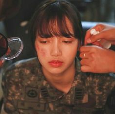 a woman is getting her makeup done by an army officer in camouflage uniform with other people around her