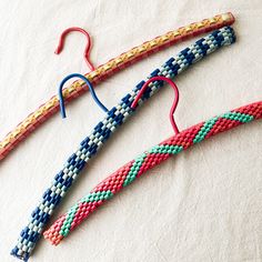 three pairs of colorful beaded earrings hang from hooks on a white surface, one with blue and red beads