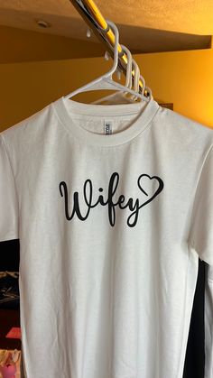 Get ready to rock your wedding with this stunning Wifey Tee! This T-shirt is perfect for any bride or wife-to-be who wants to show off her status in style. Made for women of all sizes, this white T-shirt comes with tags and features the word "Wifey" printed in bold letters, making it an ideal choice for any wedding ceremony or reception.  The tee is available in regular size and can be paired with any bottom of your choice, be it a skirt, jeans, or shorts. The bright white color of the T-shirt is perfect for any occasion, be it a formal or a casual event. Get ready to make a statement with this beautiful Wifey Tee and show off your love in style! White Bridal T-shirt With Short Sleeves, White Fitted T-shirt For Bachelorette Party, White Short Sleeve Bride T-shirt, Bride's White Short Sleeve T-shirt, White T-shirt For Bridal Shower Short Sleeve, White Short Sleeve T-shirt For Bridal Shower, White Crew Neck Top For Bridal Shower, Fitted White T-shirt As Gift, Fitted White Top For Bridal Shower