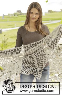 a woman is holding up a crocheted shawl in front of a field