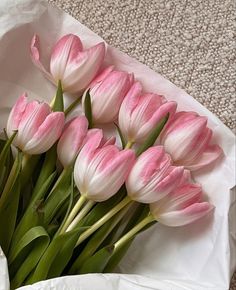 a bouquet of pink tulips in a white paper bag on the floor next to a carpeted area