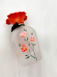 an empty glass bottle with flowers painted on the side and a red flower sticking out of it