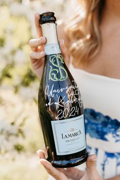 a woman holding a bottle of wine with writing on the label and in front of her