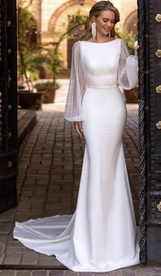 a woman standing in front of an open door wearing a white dress with sheer sleeves