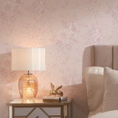 a nightstand with a lamp on top of it next to a pink flowered wallpaper